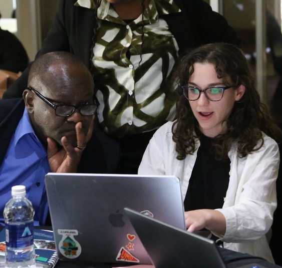 Alana Ginsburg working on a computer, surrounded by people