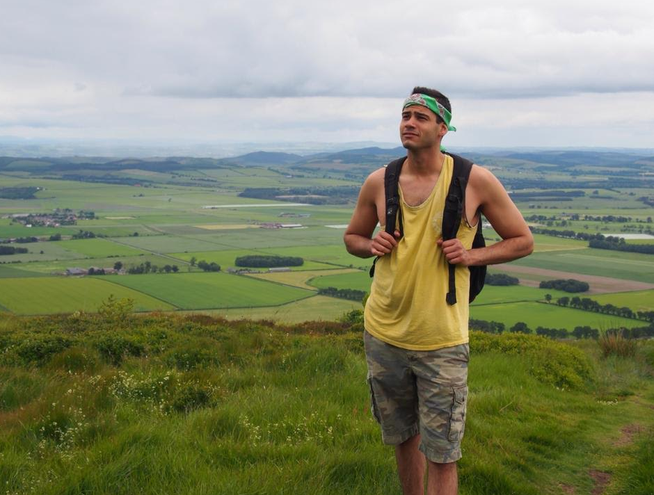 Taylor Oshan wearing a backpack with a hilly landscape as the background