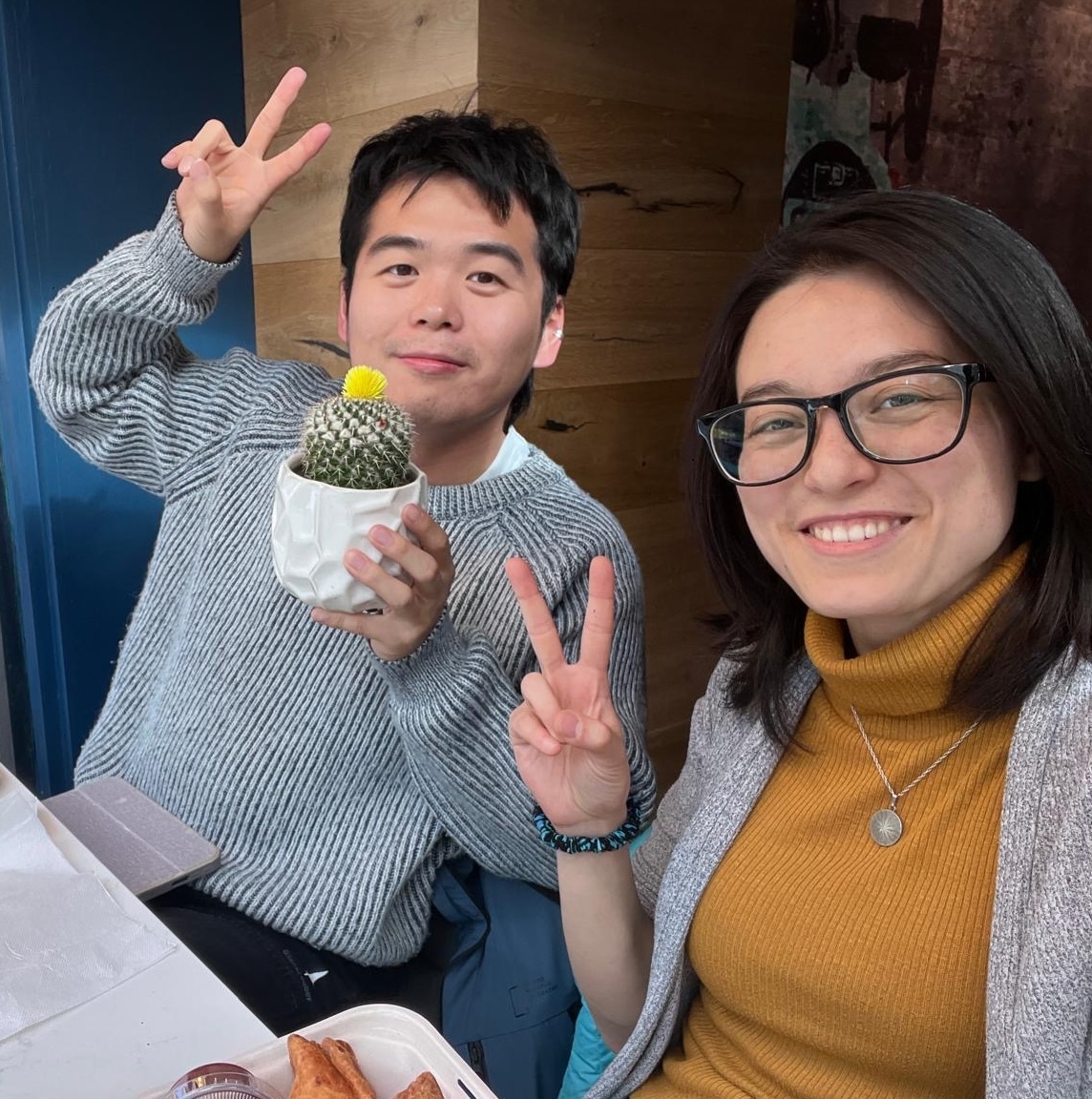 A table setting featuring two people smiling and doing the "v" peace sign with their fingers, accompanied by a decorative cactus nearby.