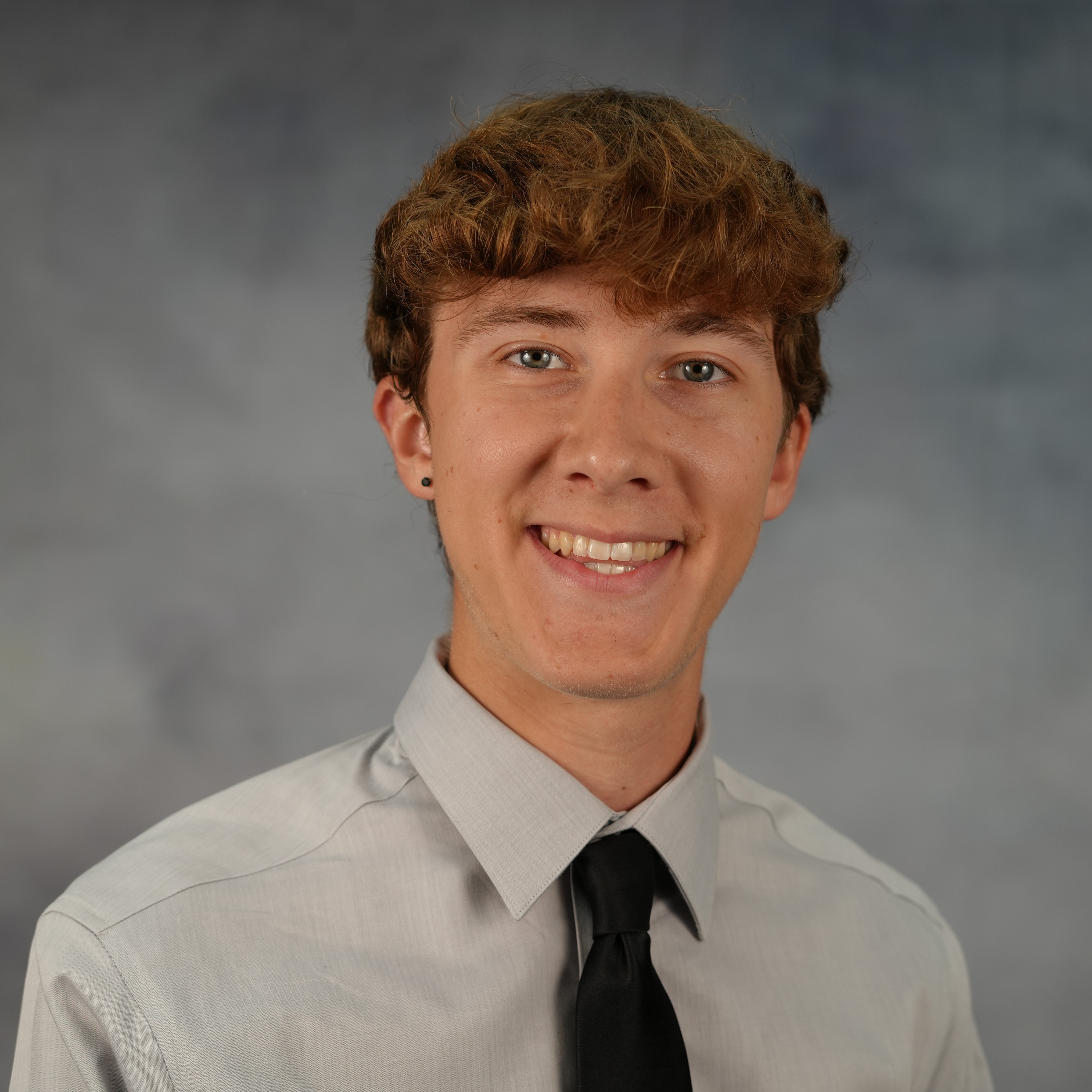 Young man smiles at the camera, wearing a long-sleeved shirt and a tie