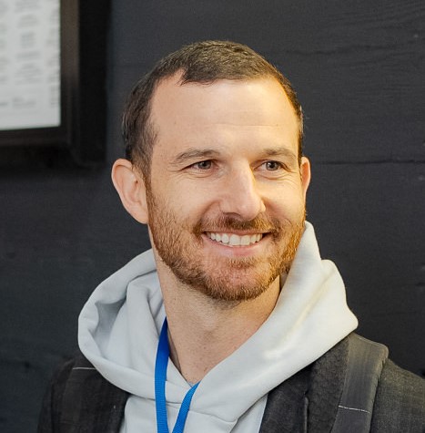 A smiling man with a beard wearing a white shirt, exuding a friendly and approachable demeanor.