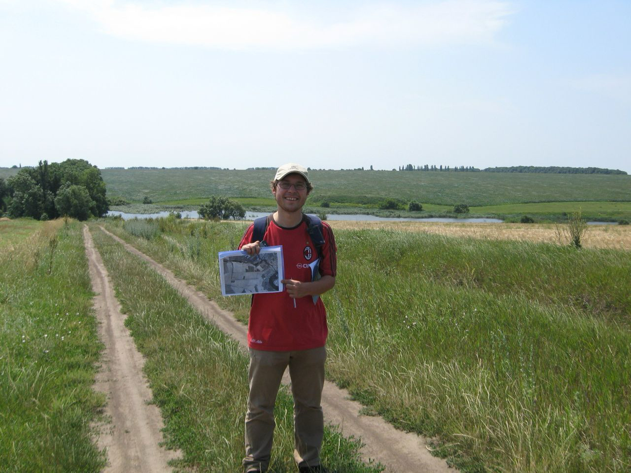 A man stands outdoors next to a large brown wooden Kansas Historical Marker sign titled 