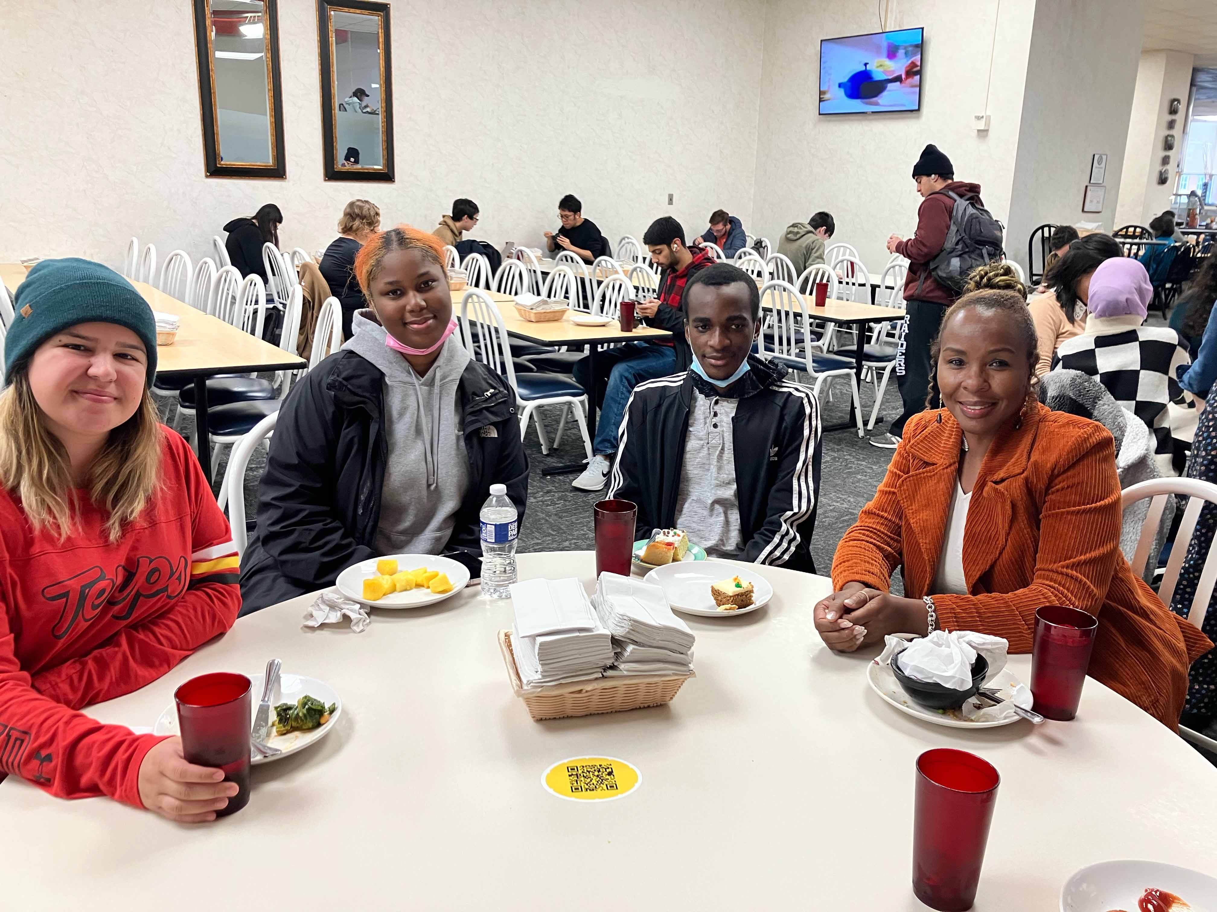 A GEOG volunteer with two high school students and a teacher eat lunch in a dining hall