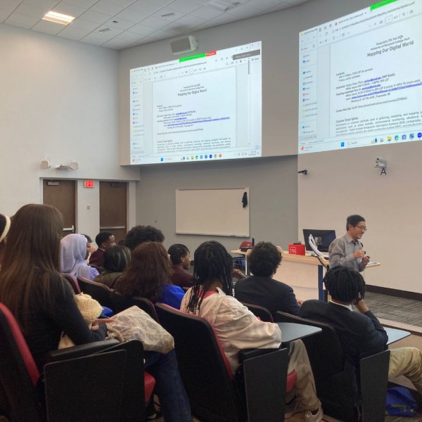 Senior lecturer Naijun Zhou delivers a presentation to an attentive GEOG473 class , highlighting key points with gestures.