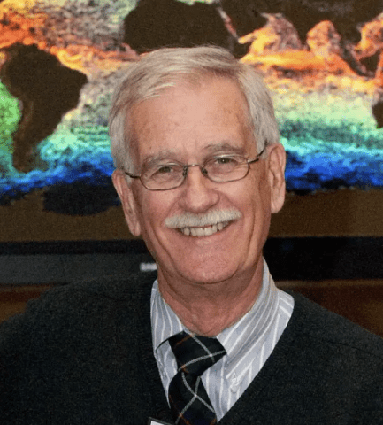Adjunct Professor Compton J. Tucker with glasses and a sweater smiles at the camera.