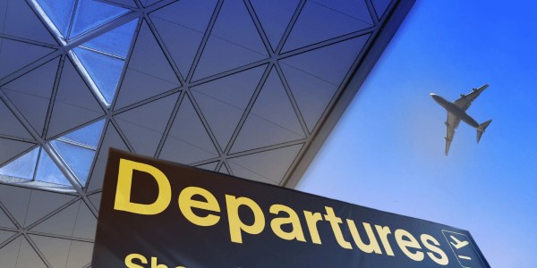 An airport sign displaying departures, with an airplane soaring overhead.