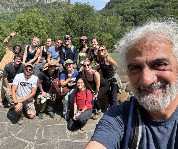 A diverse group of people happily taking a selfie in front of a scenic mountain landscape.