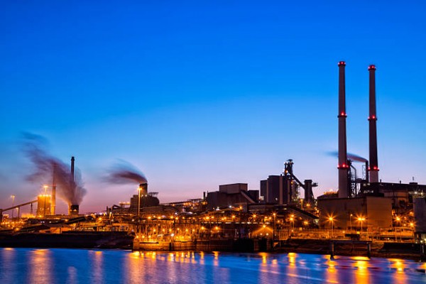 Industrial plant at dusk, with smoke billowing from chimneys against a darkening sky.