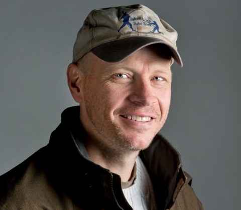 A man wearing a baseball cap and a jacket poses, reflecting a relaxed and sporty appearance.
