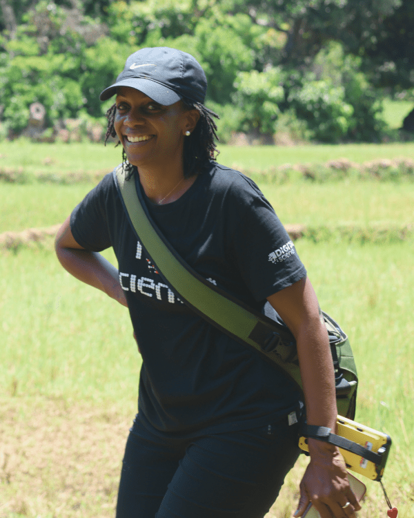 A woman with a backpack strolls across a vibrant green field under a clear sky.