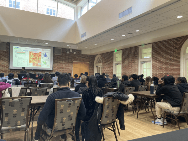 Audience watches a person on a stage showing a map projected on the wall
