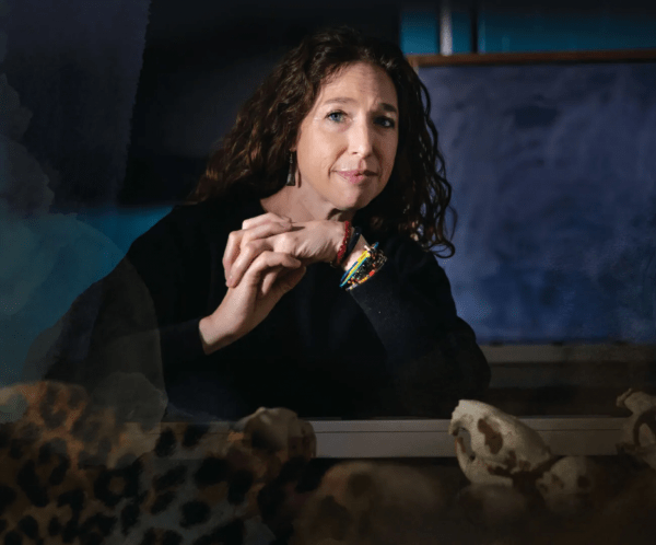 Portrait of a woman with curly hair leaning over a display of animal skulls in a workshop or laboratory
