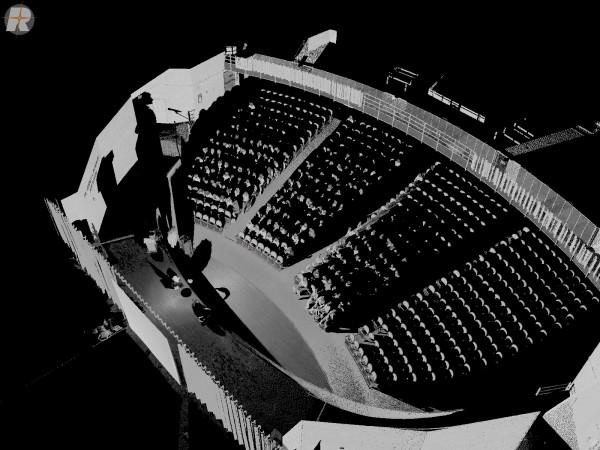 Elevated 3D laser scan (point cloud) of a school auditorium filled with an audience, showing the stage in the foreground and curved seating sections in grayscale.