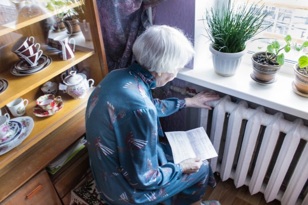 Elderly woman, holding a bill, leans over a radiator.