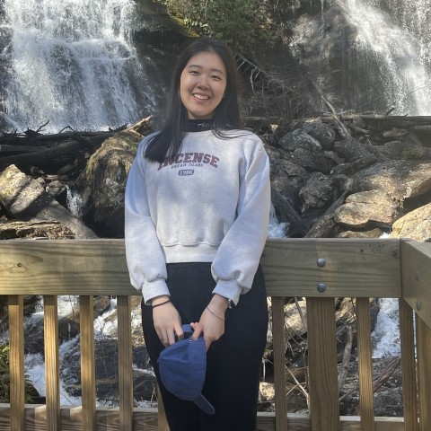 Wen Qi smiles while posing in front of a waterfall.