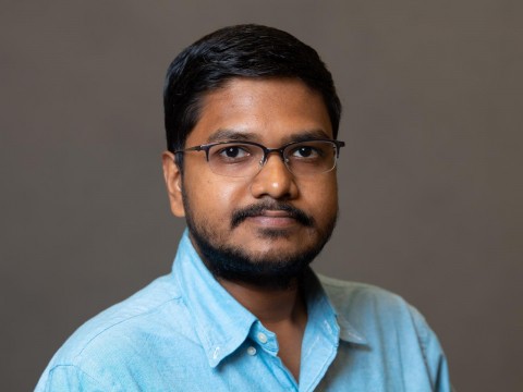 Gokul Iyer wears a blue shirt and glasses, looking directly at the camera with a neutral expression.