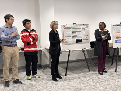 Two professors and two students stand by research posters.