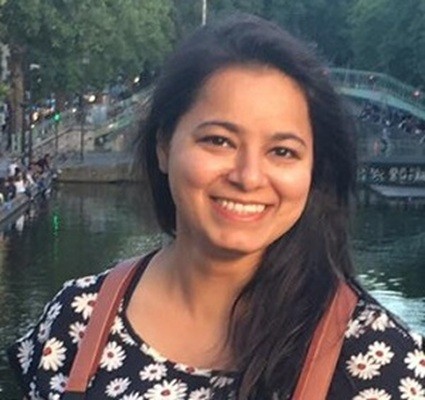 A smiling woman waring a flowering dress stares at the camera.