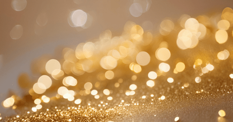 A festive, wide-angle shot featuring a shimmering field of gold glitter in the foreground that transitions into a soft, warm bokeh effect. Dozens of glowing, out-of-focus light orbs in shades of gold, cream, and white float against a blurred beige background, creating a celebratory and elegant atmosphere.