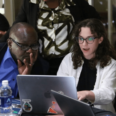 Alana Ginsburg working on a computer, surrounded by people