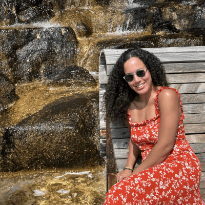 Kristen Halliday, wearing darc sits on a bench in front of waterfall. 