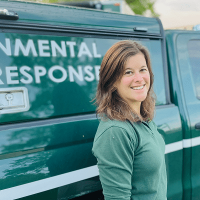 A woman stands in front of a green truck labeled "Environmental Response."