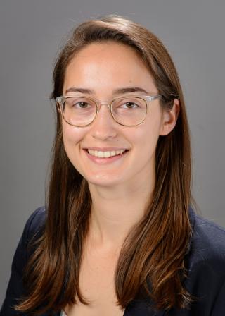 Professional headshot of Rya smiling and wearing clear glasses and a navy blazer.
